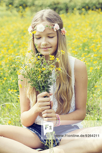 Portrait of a girl sitting on a flower meadow smelling on a bunch of flowers