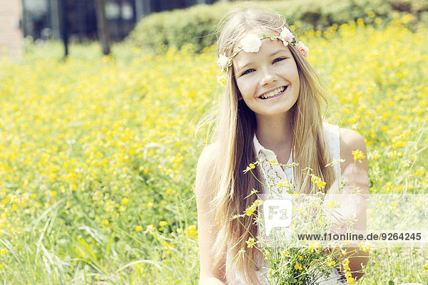 Porträt eines glücklichen Mädchens  das auf einer Blumenwiese sitzt und Blumen trägt.