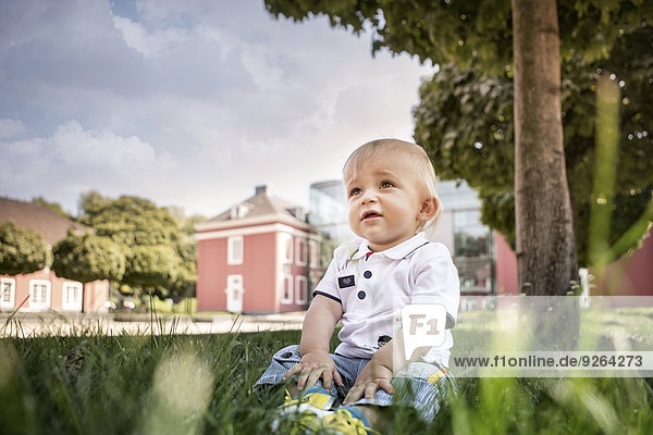 Germany Oberhausen Blond baby boy sitting in park of Oberhausen Castle