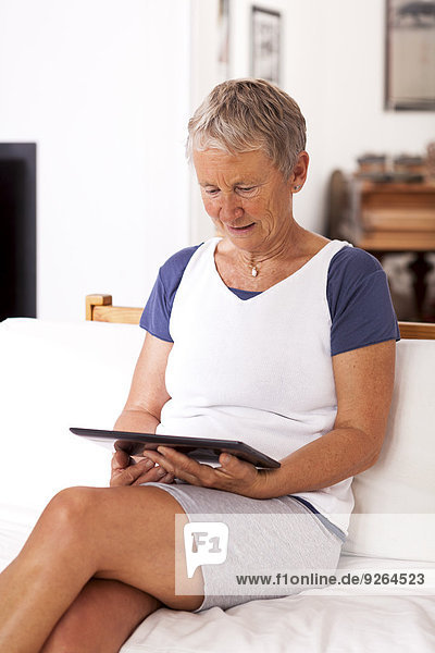 Seniorin auf der Couch sitzend mit digitalem Tablett