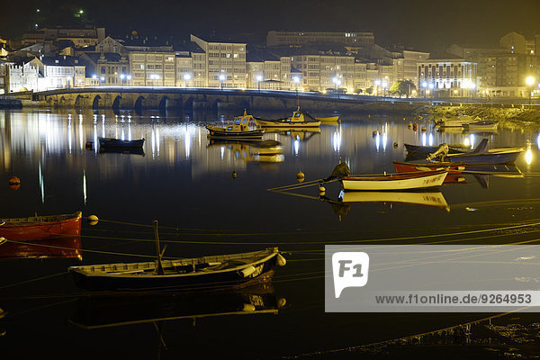 Spanien  Galizien  Viveiro  beleuchtete Brücke Ponte da Misericordia mit Booten im Vordergrund bei Nacht