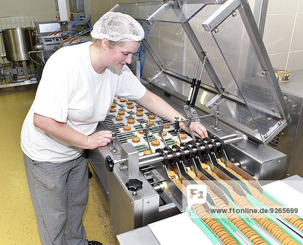 Germany  Saxony-Anhalt  woman controlling cookies on production line in a baking factory