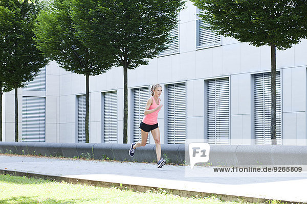 Junge Frau beim Joggen vor der Fassade eines Bürogebäudes