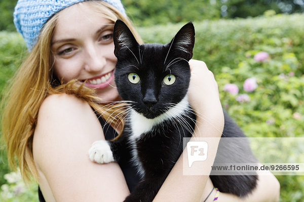 Porträt einer lächelnden jungen Frau  die eine Katze auf den Armen hält.