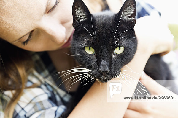 Junge Frau mit schwarzer Katze auf den Armen  Teilansicht