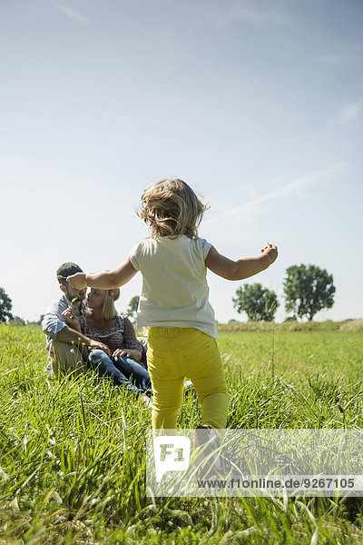 Parents and little daughter relaxing on a meadow