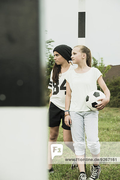 Zwei Teenagermädchen mit Fussball auf einem Fussballplatz stehend