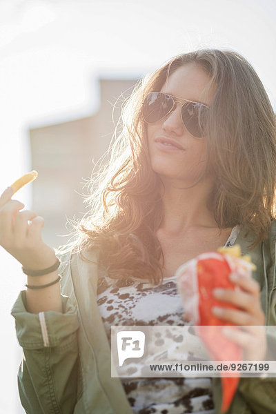 Portrait of teenage girl wearing sunglasses holding paperbag of French Fries