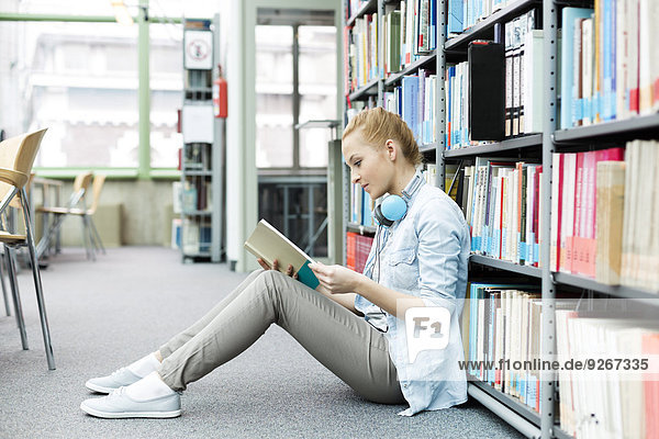 Student in a university library sitting on floor reading book