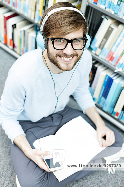 Student in einer Universitätsbibliothek auf dem Boden sitzend mit Kopfhörer