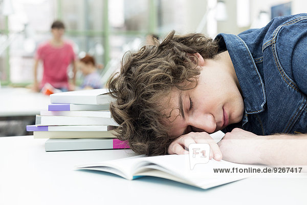 Erschöpfter Student schläft in einer Universitätsbibliothek