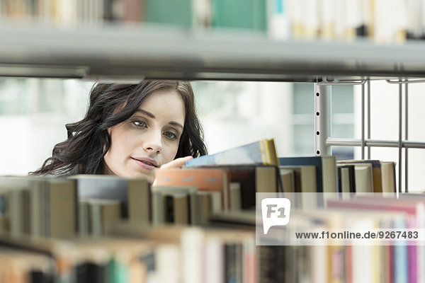 Student in einer Universitätsbibliothek nimmt Buch aus dem Regal