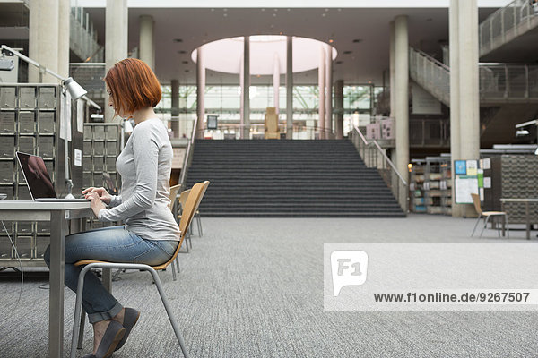 Student mit Laptop in einer Universitätsbibliothek