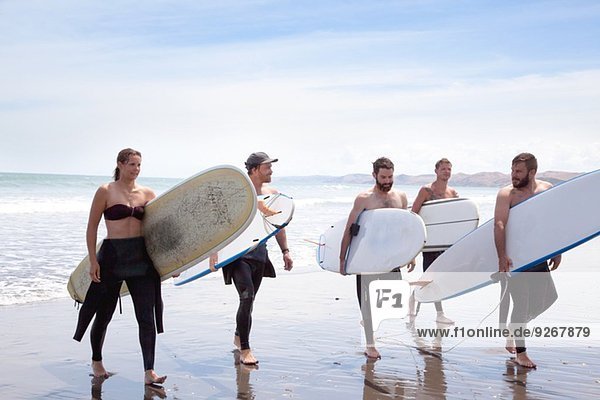 Gruppe von männlichen und weiblichen Surferfreunden,  die mit Surfbrettern vom Meer weggehen.