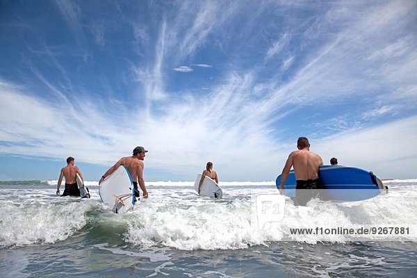 Gruppe von männlichen und weiblichen Surferfreunden  die mit Surfbrettern ins Meer waten.
