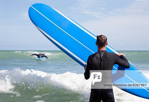 Rückansicht des männlichen Surfers mit Surfbrettbeobachtung Freund Surfen