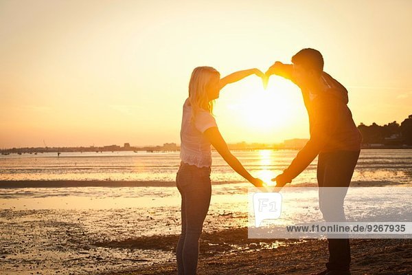 Paar bildende Herzform mit Armen am Strand bei Sonnenuntergang
