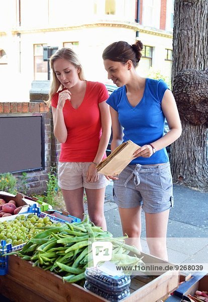 Zwei junge Frauen betrachten Gemüse am Marktstand