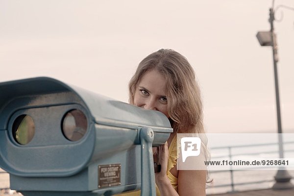 Junge Frau versteckt sich hinter einem Münzfernglas am Santa Monica Pier Kalifornien USA