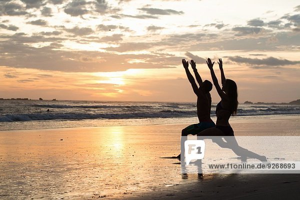 Couple doing stretching exercises on beach at sunset  Nosara  Guanacaste  Costa Rica