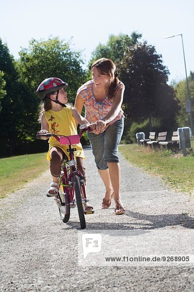 Young girl learning to ride bicycle with mother
