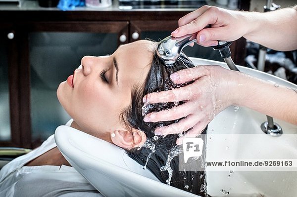 Female hairdresser rinsing young woman's hair in hair salon