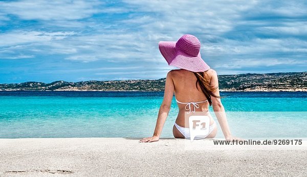 Rückansicht der jungen Frau mit Bikini und Sonnenhut am Strand  La Maddalena  Sardinien  Italien