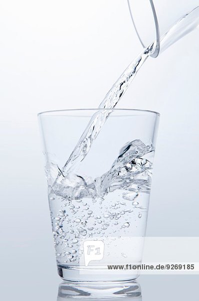 Klares Wasser,  das aus der Kanne in das Trinkglas fließt