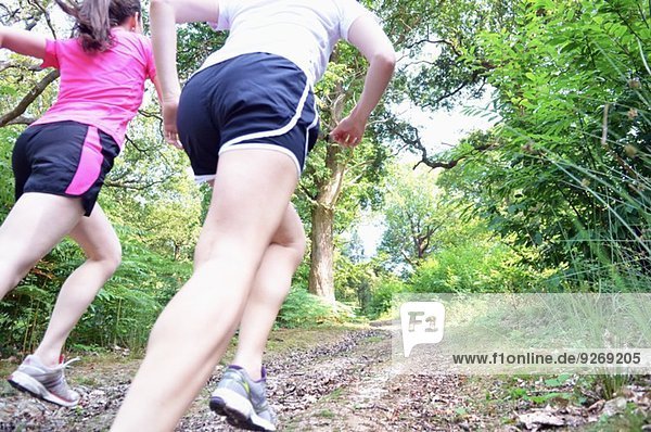Close up of two young women runners running along forest track