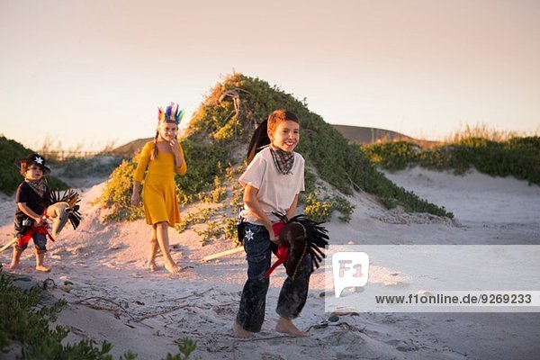 Three children dressed as native american and cowboys running in sand dunes