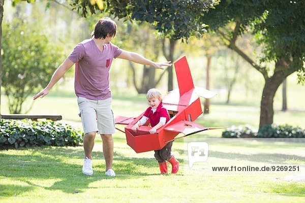 Vater und Sohn laufen mit Spielzeugflugzeug im Park