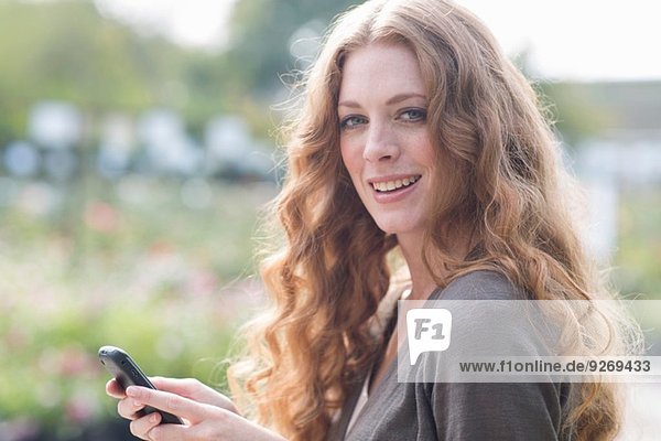 Porträt einer jungen Frau  die auf einem Smartphone im Garten schreibt