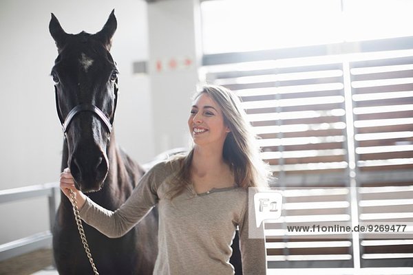 Young woman leading black horse in stables