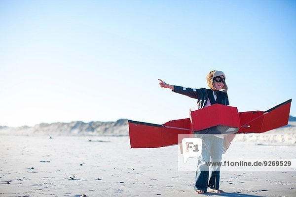 Junge steht mit einem Spielzeugflugzeug und zeigt auf den Strand.