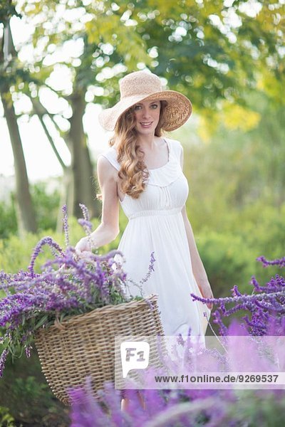 Porträt einer schönen jungen Frau auf der Wiese  die einen Korb mit violetten Blumen trägt.