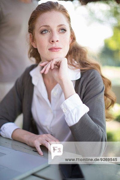 Young businesswoman with hand on chin at garden table