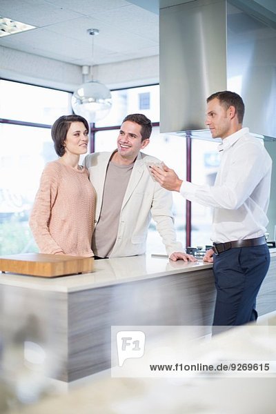 Verkäufer und mittleres erwachsenes Paar beim Betrachten von Keramikfliesen im Küchen-Showroom