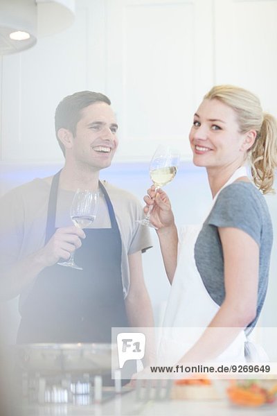 Couple preparing food and drinking glass of white wine in kitchen