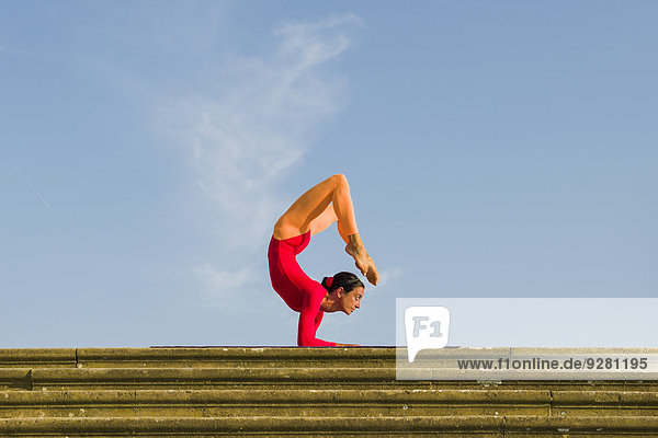 Junge Frau praktiziert Hatha-Yoga im Freien  in Vrischikasana-Haltung  Skorpion-Pose