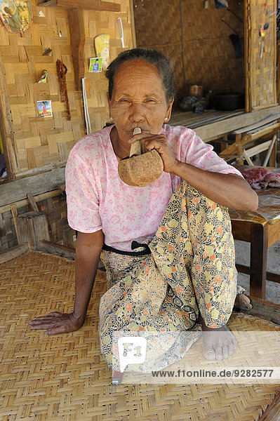 Burmese woman smoking a cheroot  Burmese cigar  in a traditional farmhouse  made of wood and bamboo  Bagan  Central Mynamar  Myanmar
