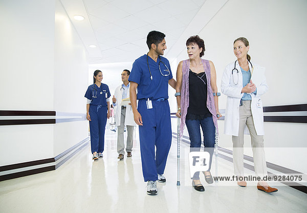 Doctor and nurse walking patient down hospital hallway