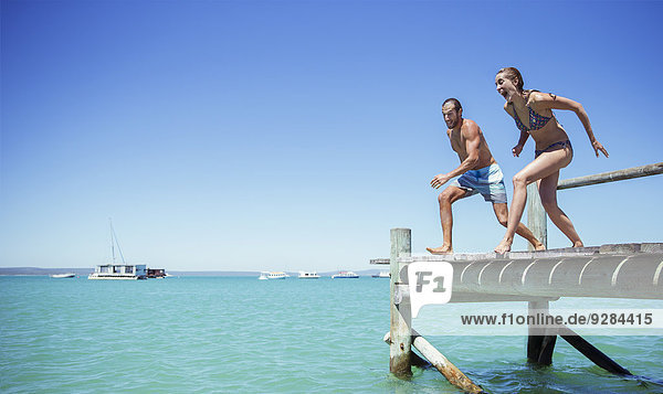Couple jumping off wooden dock together