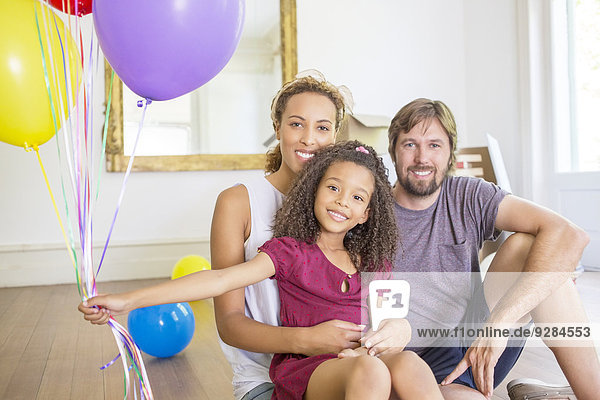 Familie sitzend im Wohnraum mit Luftballons