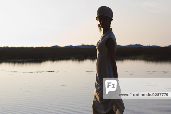 Junge Frau im Kleid vor dem See in der Abenddämmerung