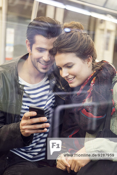 Young couple riding subway looking at digital tablet together