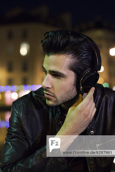 Young man outdoors at night listening to music with headphones
