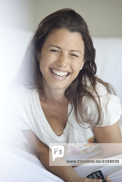 Woman laughing while watching TV in bed