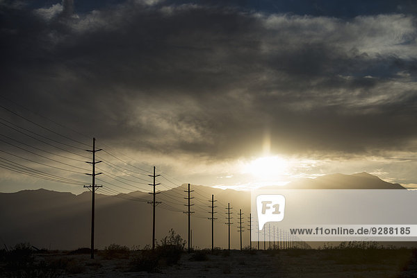 Stromleitungen in Reihen quer durch die Landschaft  vor einem sich verdunkelnden Himmel.