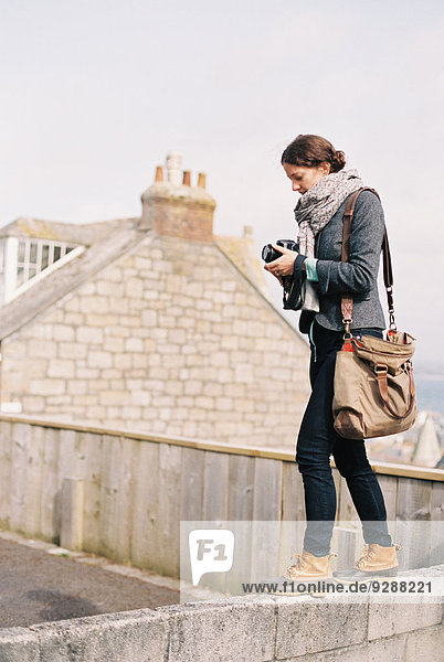 Eine Frau mit einer großen Tasche  die einen Fotoapparat hält  steht oben auf einer Mauer.