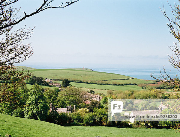 Blick von einer Hügelspitze über ein Dorf im Tal  mit Blick auf das Meer von der Küste aus.